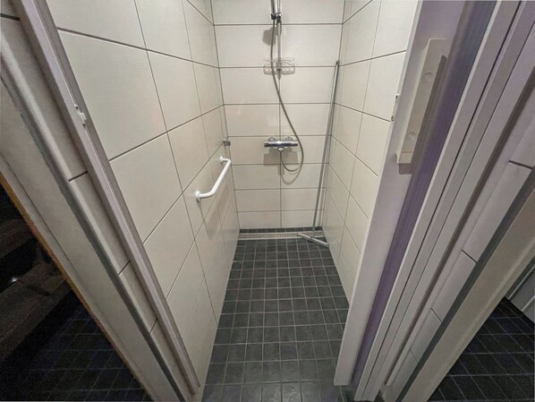 A small, tiled shower stall with a handheld showerhead and a handheld shower control.