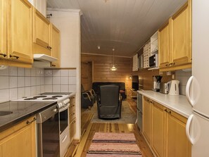 A narrow kitchen with wooden cabinets, a stove, and a microwave. - Villa siesta by Interhome (Hämeenlinna)
