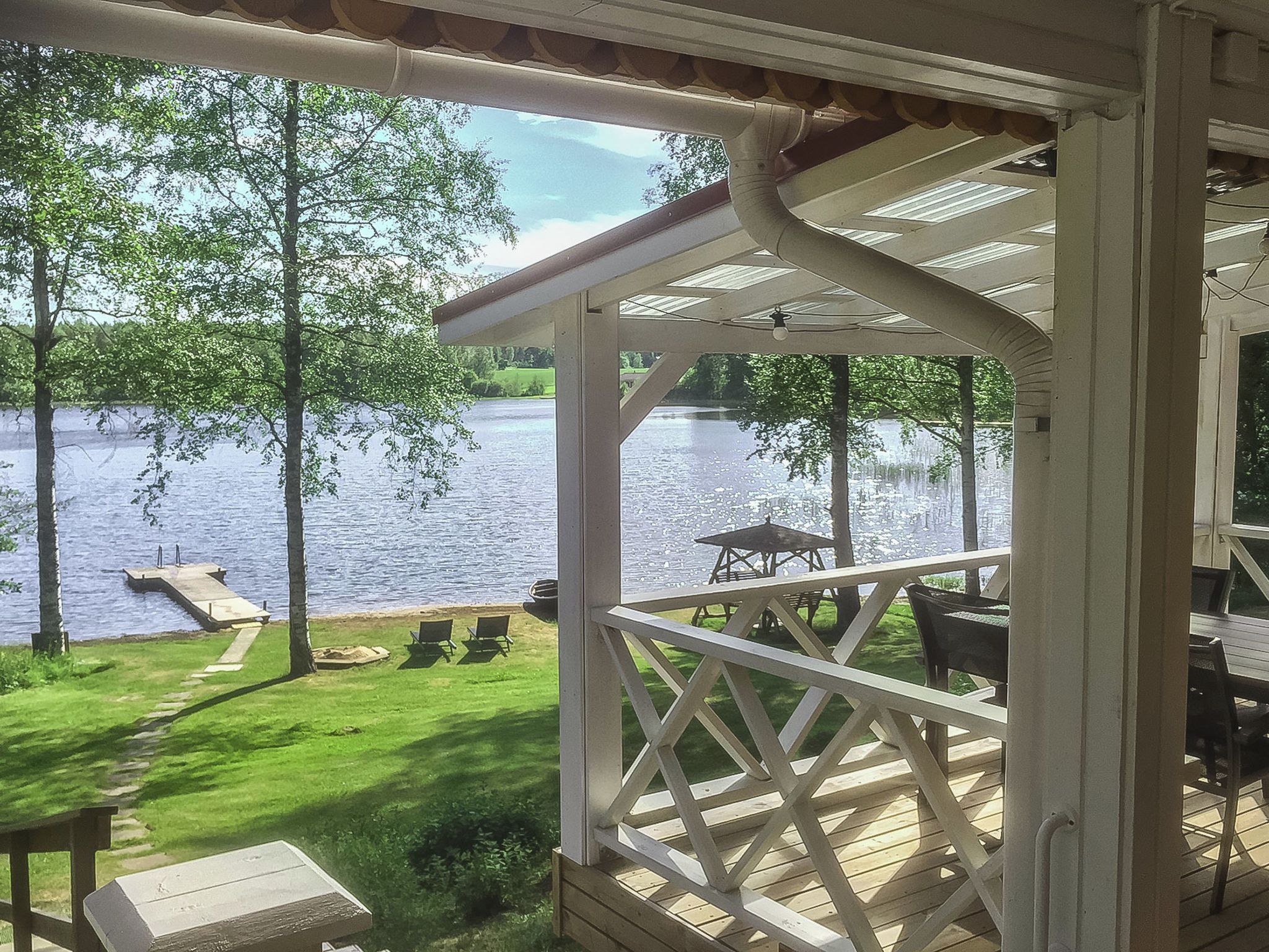 A covered outdoor area with a view of a lake, a picnic table, and lawn chairs.