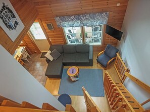Interior de madera con techos altos, un sofá seccional, un sillón azul y una pequeña mesa con un libro.