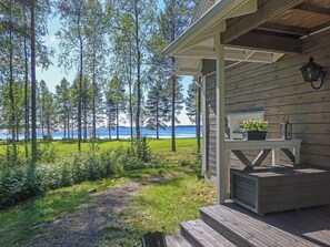 A wooden cabin with a porch overlooking a lake and forest.