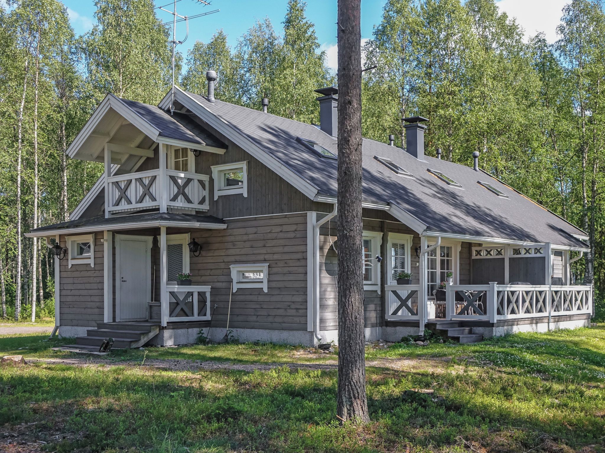 Kaksikerroksinen mökki, jossa on kuisti, savupiippu ja terassi.
