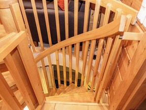 Un escalier en bois, doté d’une rampe, mène à un canapé de couleur sombre situé au fond de la pièce.