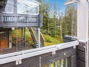 Un bâtiment en bois à deux étages, doté d’un balcon en verre, d’une terrasse en bois et d’un escalier menant à l’étage supérieur.