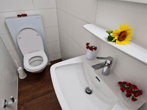 A bathroom with a toilet, sink, and a shelf with a sunflower decoration.