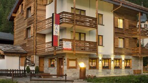 Un immeuble en bois à plusieurs étages, doté de balcons, d’une enseigne de restaurant et d’un panneau indiquant la possibilité de louer du matériel de ski.