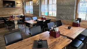 Un restaurant avec des tables et des chaises en bois, des murs en pierre et de grandes fenêtres.