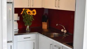 Une cuisine avec des meubles blancs, un pare-feu rouge et un vase rempli de tournesols posé sur le plan de travail.