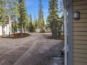 Une allée de gravier mène à une maison entourée d’une clôture en métal et bordée d’arbres.