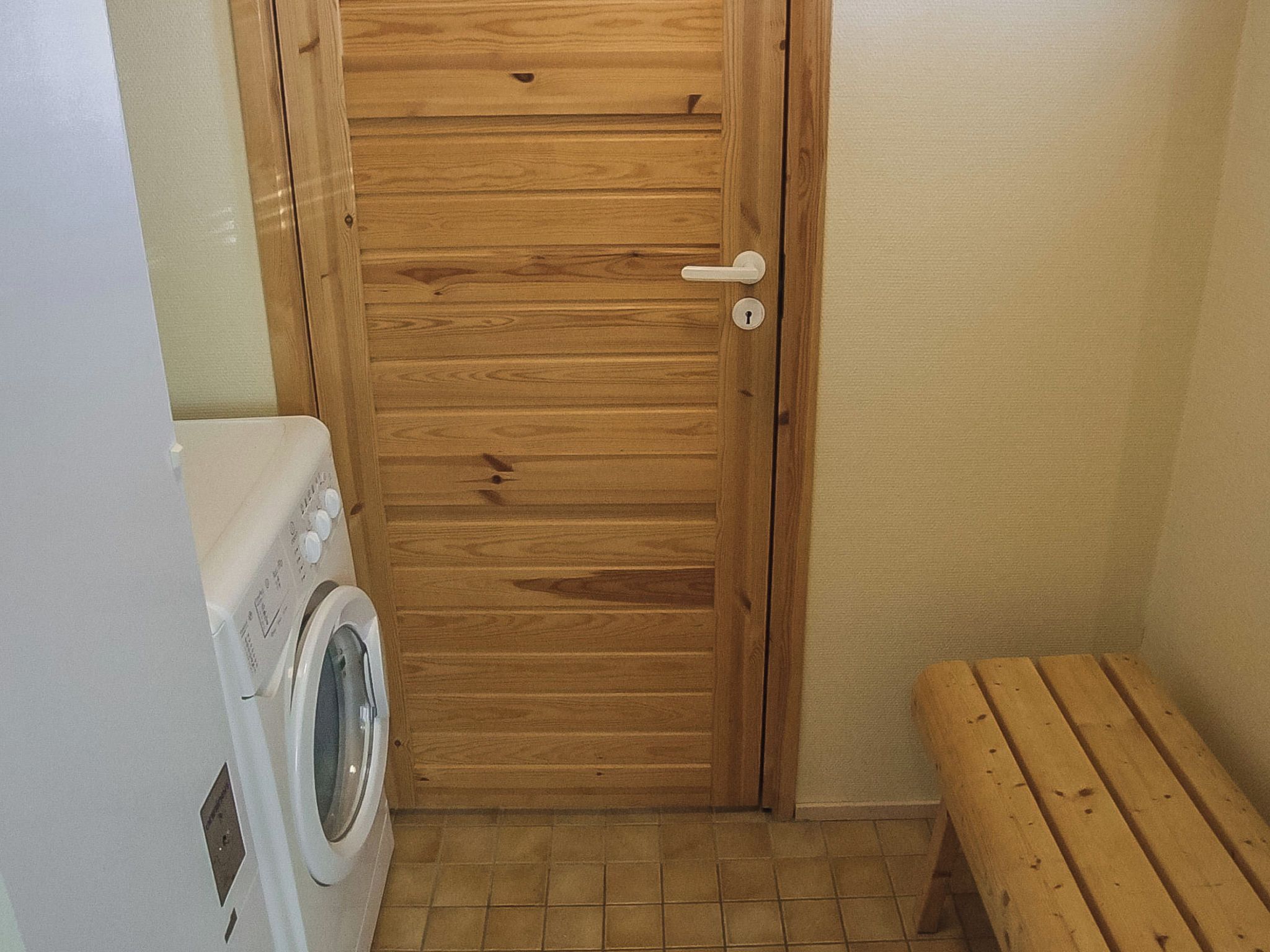 A small laundry room with a wooden door, a washing machine, and a bench.