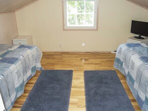 A bedroom with two beds, a window, a TV, and a small bedside table.