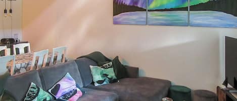En moderne stue med sofa, puder, sofabord og et maleri af nordlys.