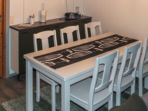 A dining area with a table set for four, a dark-colored table runner with a geometric pattern, and a radio on a cabinet.