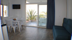 Een kamer met balkon, plafondventilator, televisie aan de muur en een eethoek met stoelen en een tafel.
