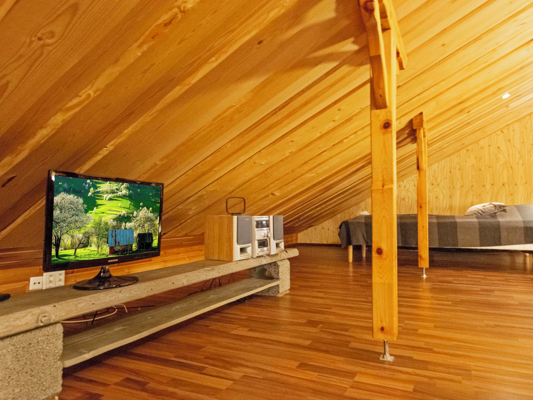 Une chambre mansardée avec une télévision posée sur une étagère en bois, un haut-parleur et un lit.