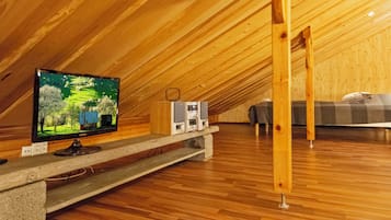 Une chambre mansardée avec une télévision posée sur une étagère en bois, un haut-parleur et un lit.