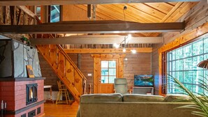 A cozy cabin interior with a fireplace, wooden walls, a staircase, and a television.