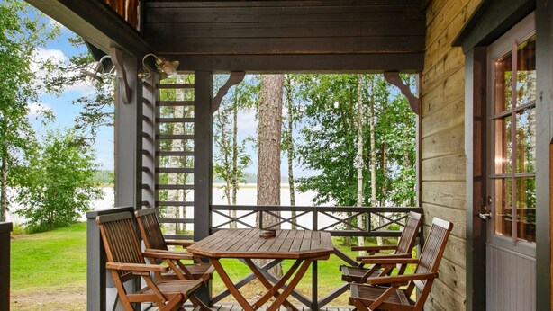 A wooden deck with a table and four chairs, overlooking a lake and trees.