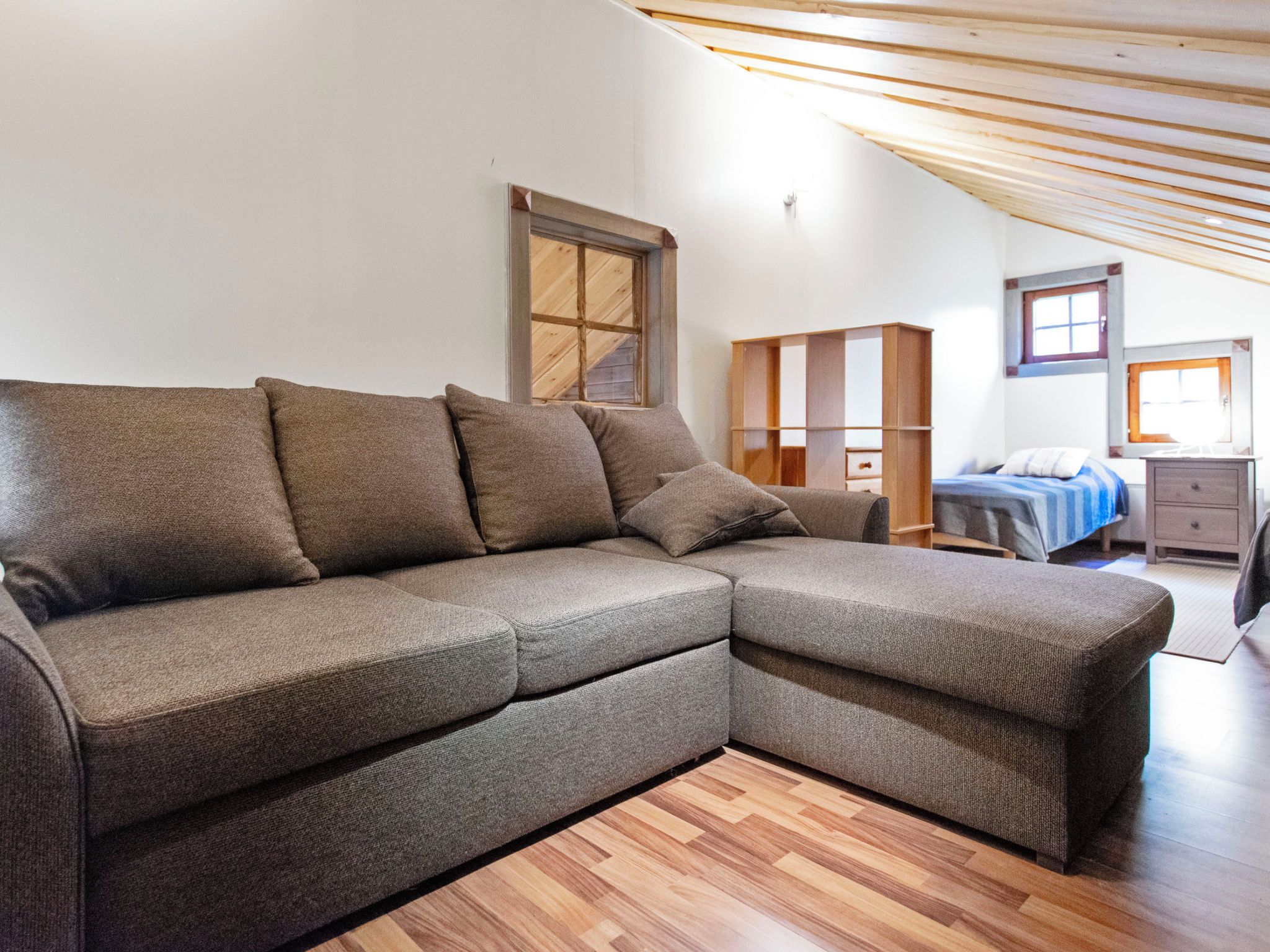 Una sala de estar moderna con un sofá seccional, techo de madera y vista al dormitorio.