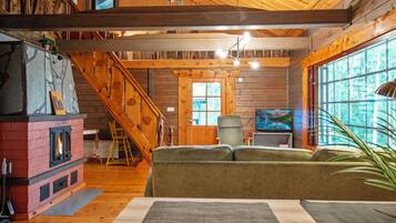 A cozy cabin interior with a fireplace, wooden walls, a staircase, a sofa, and a television.