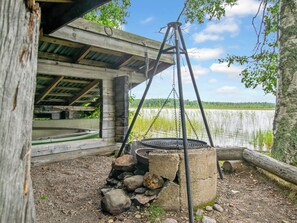 Un área de cocina al aire libre de estilo rústico con un horno de piedra, un columpio colgante y una estructura de madera con techo cubierto.