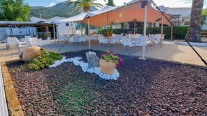 An outdoor seating area with white plastic chairs and tables, a covered section with a red roof, and a decorative arrangement of rocks and plants. - Rescator Resort 115 - One Bedroom Resort, Sleeps 4 (Roses)