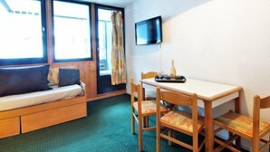 A room with a bed, a table with chairs, a TV mounted on the wall, and a window with curtains. - Le Grépon by Interhome (Chamonix)