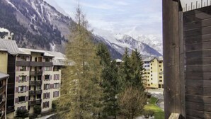 A mountain resort with multi-story buildings, a small stream, and snow-capped peaks in the background. - Le Grépon by Interhome (Chamonix)