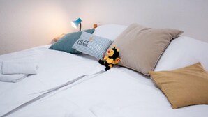 A neatly made bed with white linens, a blue pillow with text, a brown pillow, and a small toy figure. - Windrose by Interhome (Norddeich)