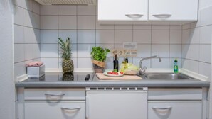 A compact kitchen with white cabinets, a stainless steel sink, and a countertop with a cutting board, a bottle of olive oil, and a potted plant. - Windrose by Interhome (Norddeich)