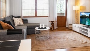 Un salon moderne avec un canapé gris, une table basse blanche et un téléviseur posé sur un meuble blanc.
