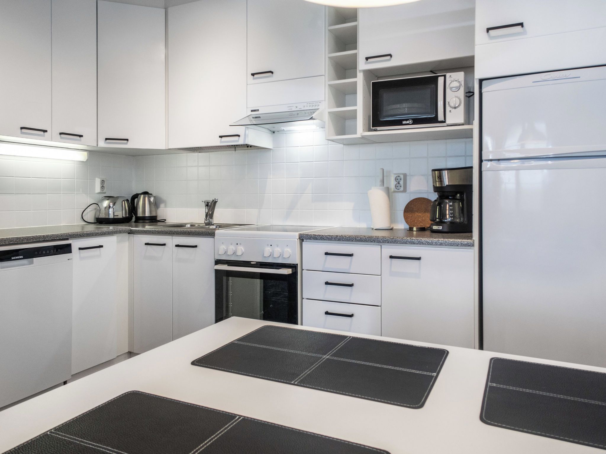 Une cuisine moderne avec des meubles blancs, un four à micro-ondes, une machine à café et un lave-vaisselle Siemens.