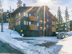 Un immeuble résidentiel à plusieurs étages, doté de balcons, avec une voiture garée devant et de la neige au sol.