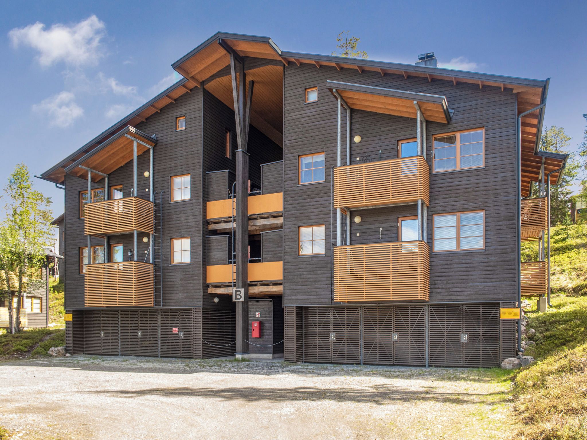 Un immeuble à plusieurs étages doté de balcons, d’un garage et d’une allée gravillonnée.