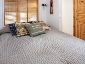 A bed with a textured grey quilt, two pillows with geometric patterns, and a wall-mounted lamp.