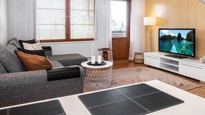 Un salon moderne avec un canapé, une table basse, un téléviseur fixé sur un mur en bois et une fenêtre avec des stores.