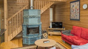 Un intérieur en bois avec une cheminée en pierre, un escalier, un canapé rouge et un téléviseur.