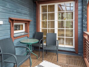 A covered outdoor seating area with a table and chairs, a window with blinds, and a wooden deck. - Syvärinkulta a by Interhome (Nilsiä)