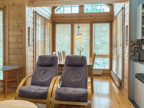 A wooden interior with two reclining chairs, a table, and a view through large windows.