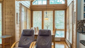 Un intérieur de chalet chaleureux avec deux fauteuils inclinables, une table à manger et une vue magnifique grâce à de grandes fenêtres.