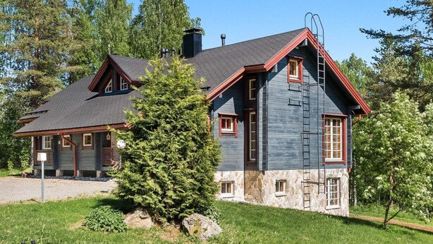 Une maison à deux étages, avec des fondations en pierre, une façade de couleur gris foncé et des éléments décoratifs rouges.