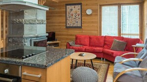 L’intérieur d’un chalet chaleureux, avec une cheminée en pierre, un canapé rouge et un plafond en bois.