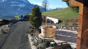 A rustic wooden building with a stone foundation, a wooden barrel, and a car parked outside. - Ferienhaus Niesen View by Interhome (Erlenbach)