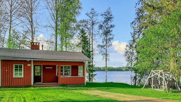 Uma cabana vermelha com varanda, balanço e vista para o lago.