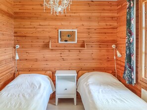 Ein Zimmer in einer Holzhütte mit zwei Betten, einem kleinen weißen Nachttisch, einer Wanduhr und einem Kronleuchter.
