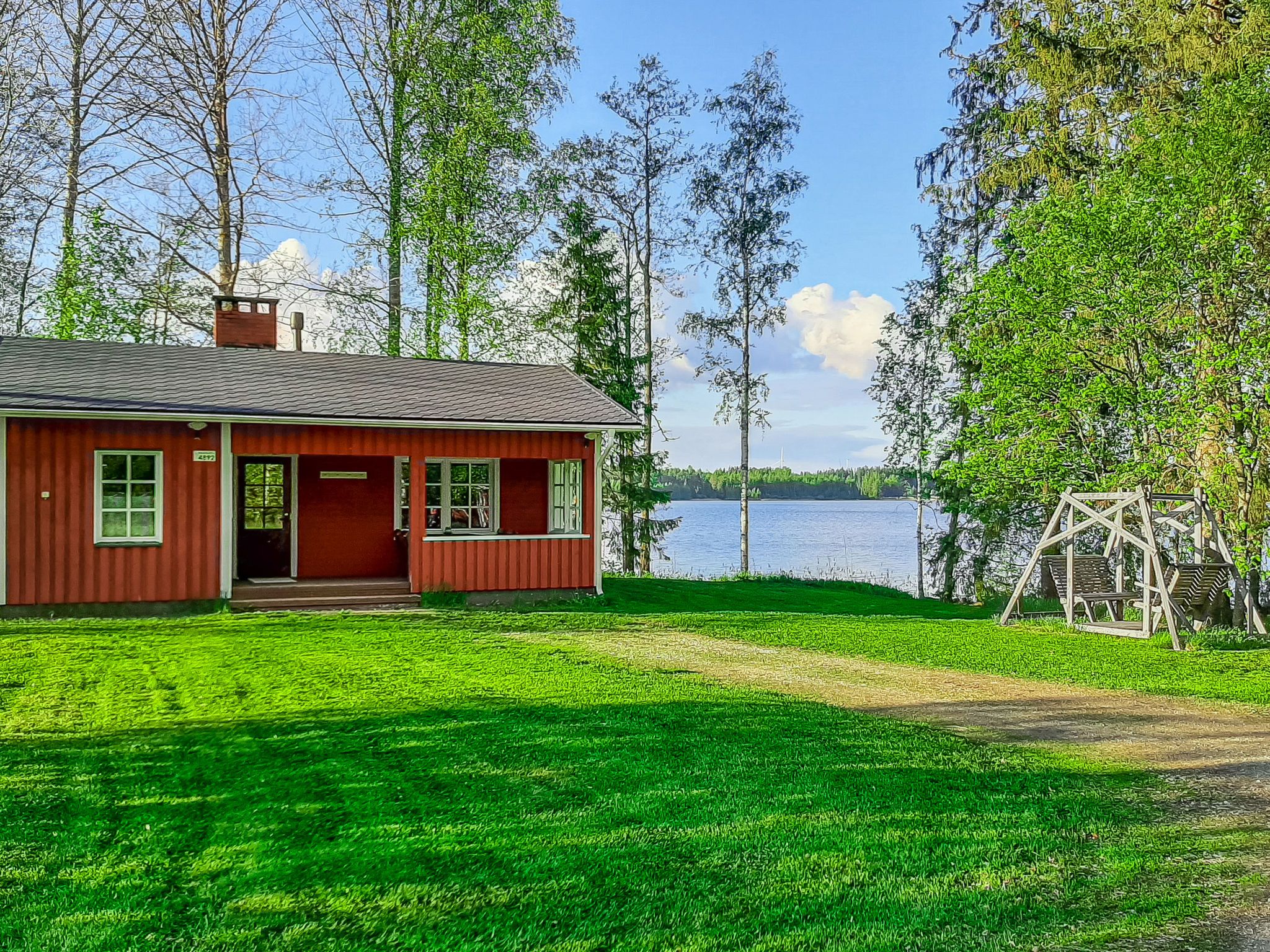 Punainen mökki, jossa on kuisti, nurmikkoinen piha ja näkymä järvelle.