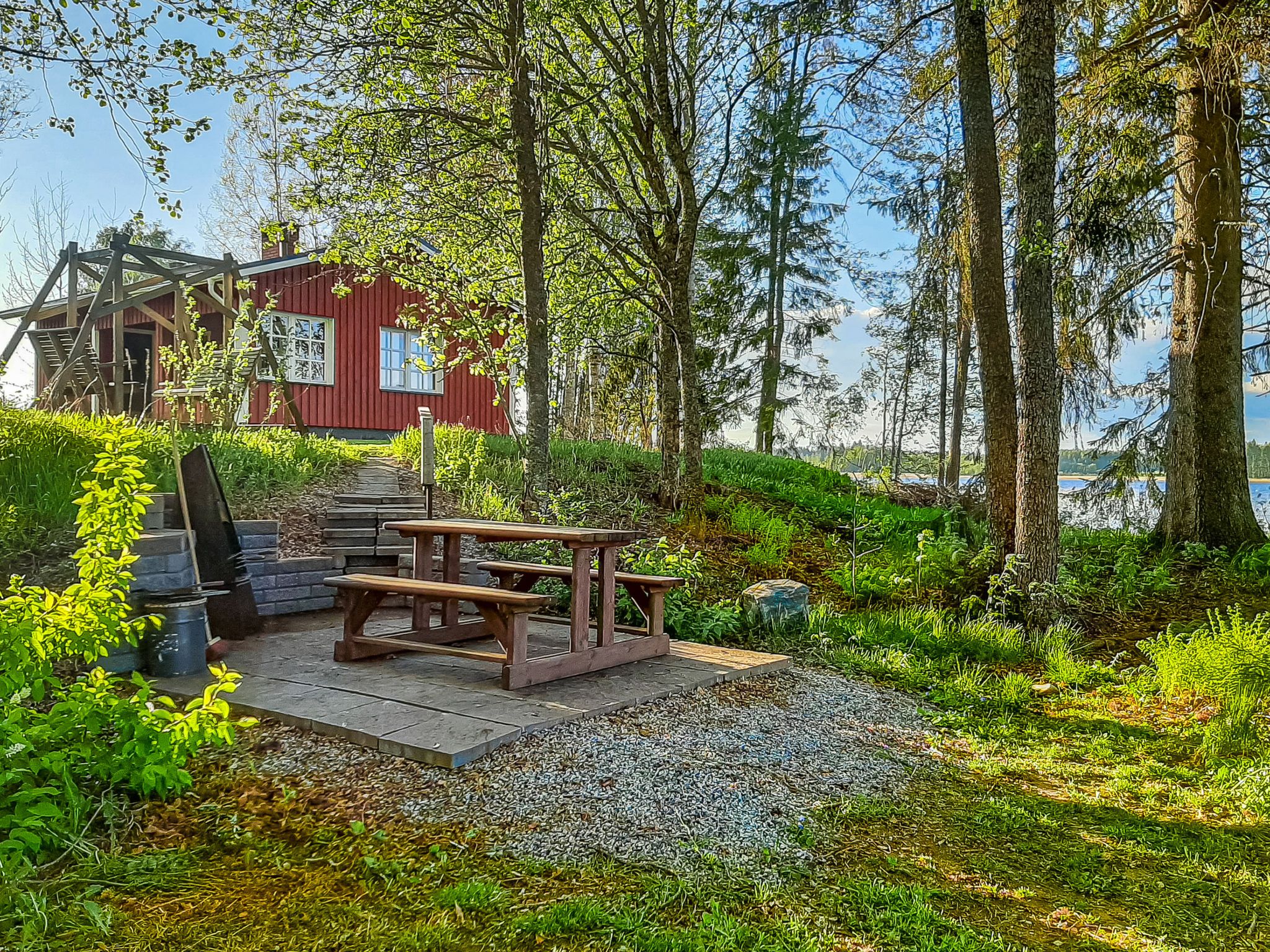 Ein Holztisch mit Bänken, ein rotes Gebäude und ein bewaldetes Gebiet mit Blick auf das Wasser.