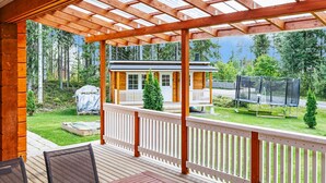A wooden deck with a pergola, a small house with a porch, and a trampoline in a wooded area. - Aapeli iso by Interhome (Ähtäri)