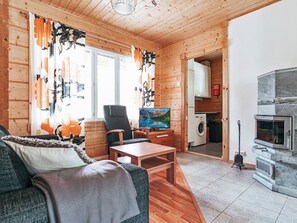 A cozy log cabin interior with a sofa, chairs, a television, a fireplace, and a kitchen area. - Aapeli iso by Interhome (Ähtäri)
