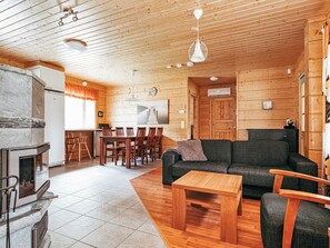 A cozy cabin interior with a fireplace, wooden dining table, sofa, and a kitchen area. - Aapeli iso by Interhome (Ähtäri)
